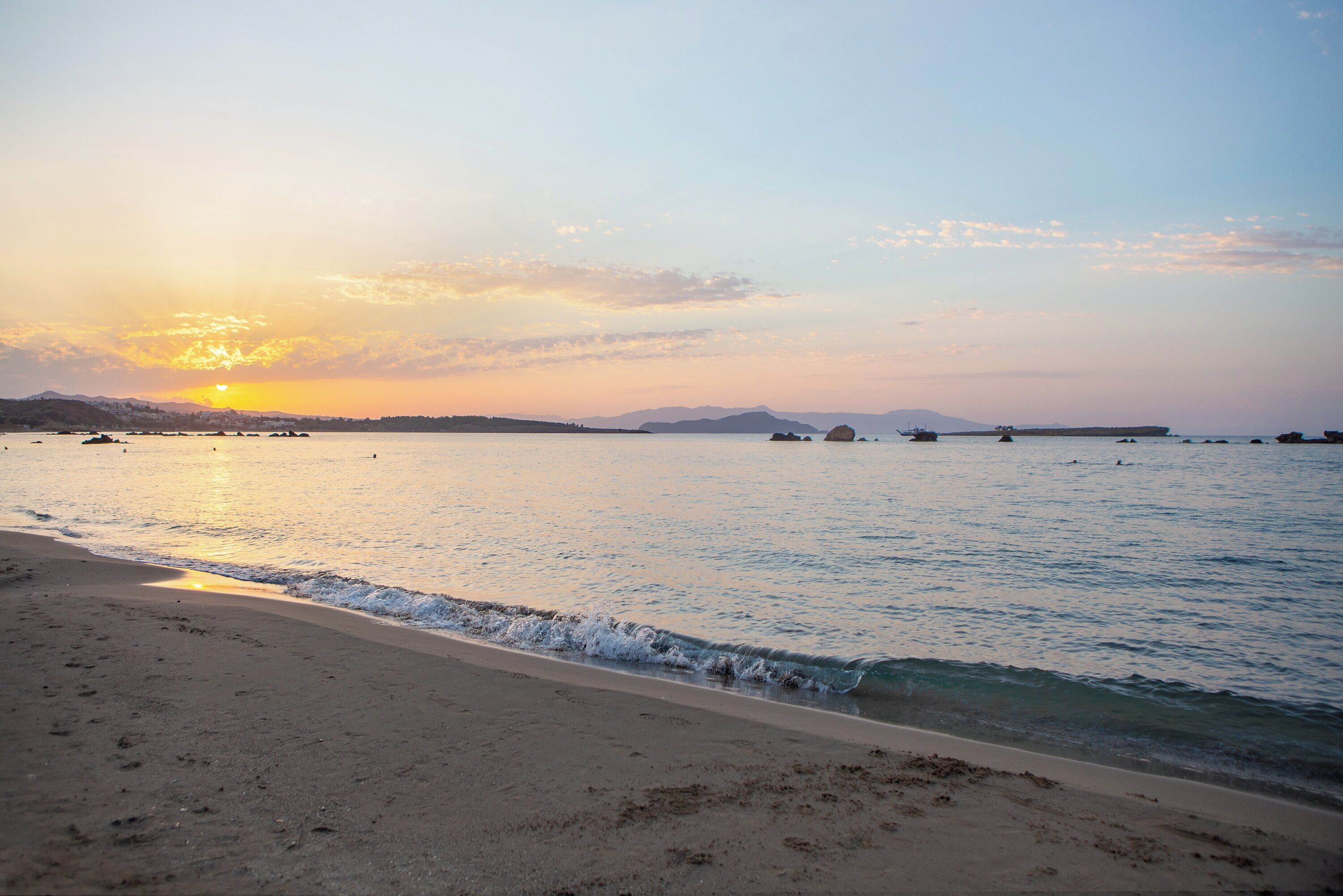 A beach with calm waters, a clear sky, and distant mountains.