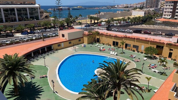 A rooftop pool area with a clear view of the sea and a large building in the background. - Views of Los Cristianos pier. Pier View. (LOS CRISTIANOS)