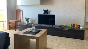A modern living room with a dark wood TV stand, a small table with a vase and remote, a chair, and a potted plant. - Views of Los Cristianos pier. Pier View. (LOS CRISTIANOS)