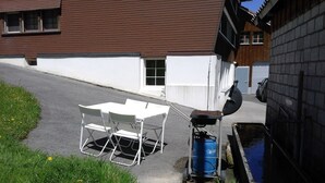 Mesa y sillas blancas colocadas al aire libre junto a un edificio con techo marrón y paredes blancas.