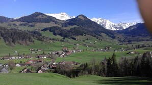 Un pueblo rural con casas dispersas entre colinas verdes onduladas, rodeado de montañas con cumbres nevadas.