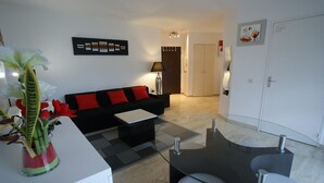Una sala de estar moderna con un sofá negro, cojines rojos, una mesa de centro de cristal y una planta.