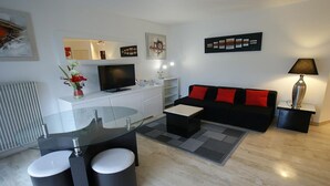 Una sala de estar moderna con un sofá negro, una mesa de comedor de cristal, un televisor y una lámpara.