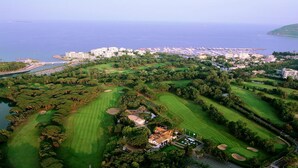 Vista aérea de un campo de golf con múltiples zonas verdes, un club de campo y un puerto deportivo.