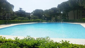 Una piscina rectangular con borde de azulejos, rodeada de jardines y árboles bien cuidados.