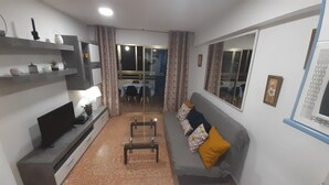 A compact living space with a sofa, a TV, a small table, and a window.
