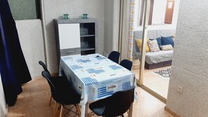 Pieni ruokailutila, jossa on sinivalkoruudullinen pöytäliina, kaksi mustaa tuolia ja valkoisella ovella varustettu kaappi.