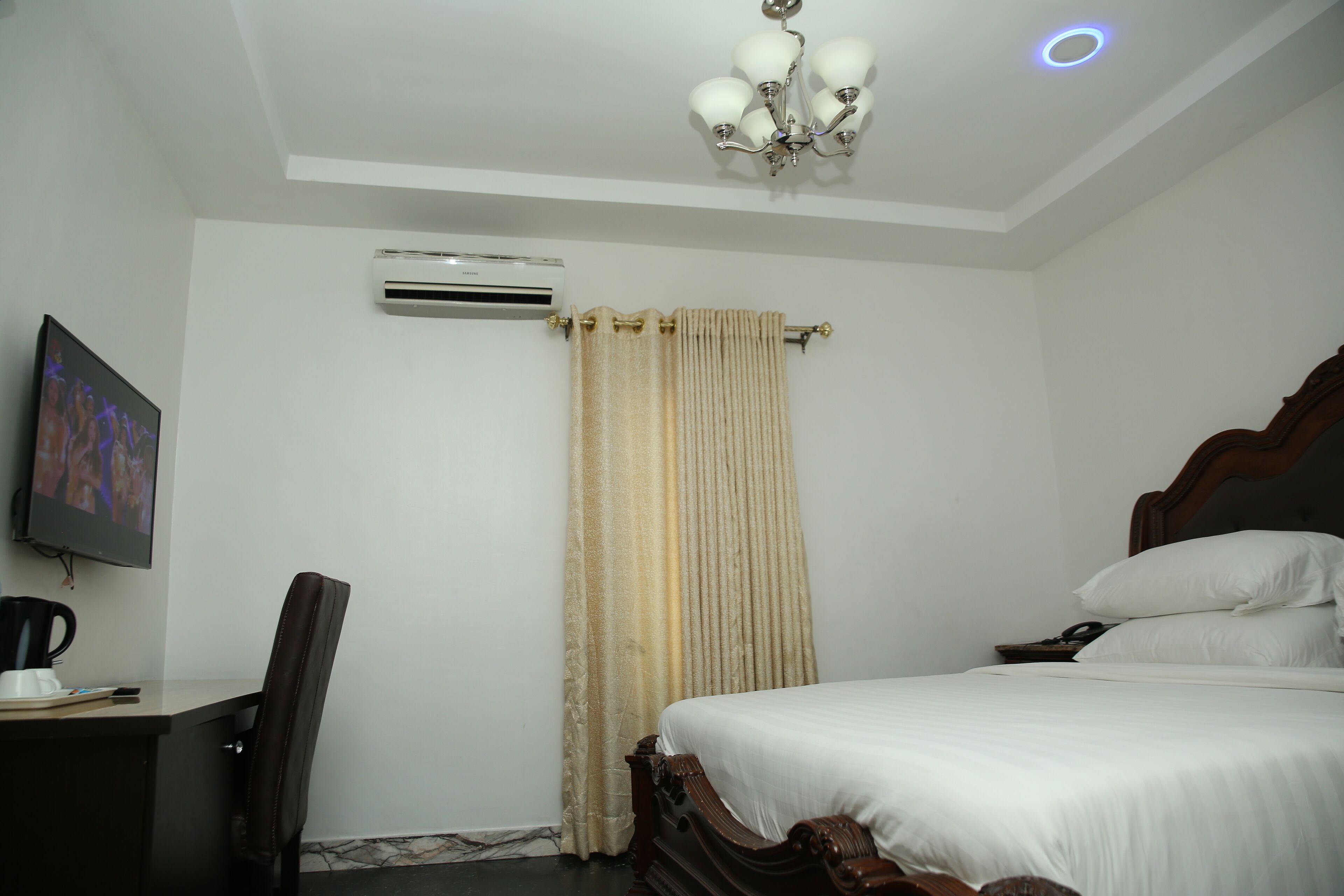 Una habitación de hotel con una cama, un escritorio con silla, televisor, aire acondicionado y una cortina.