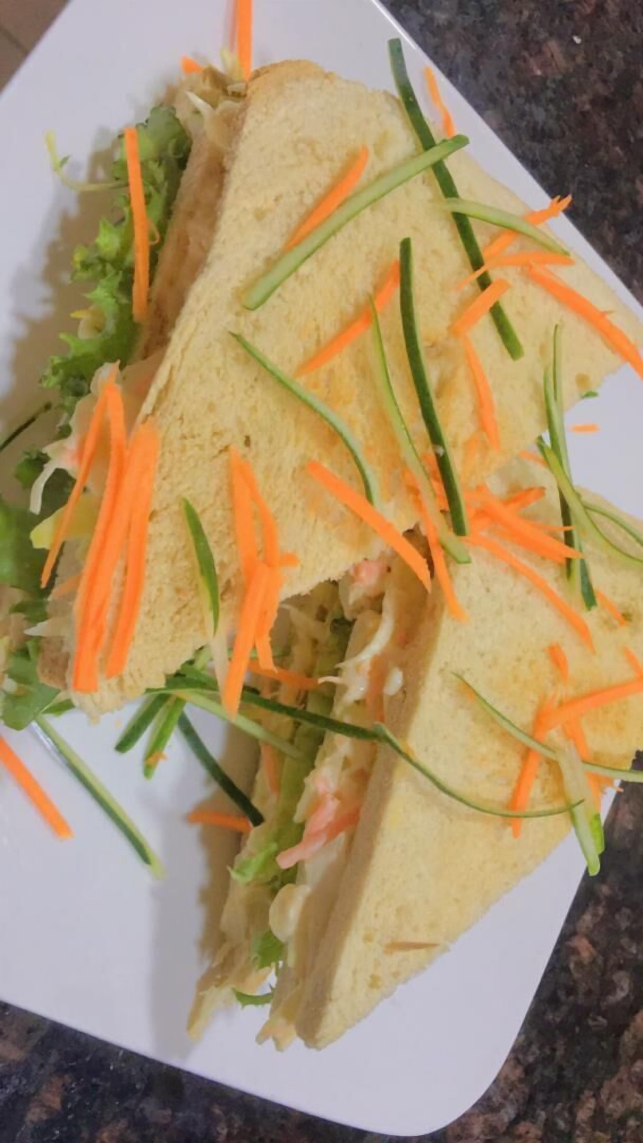 A sandwich with lettuce, carrots, and green onions on a white plate.