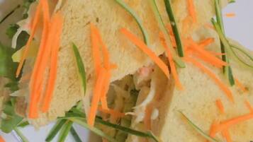 A sandwich with lettuce, carrots, and green onions on a white plate.
