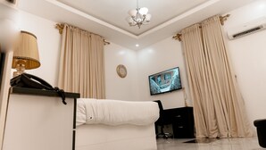 Una habitación de hotel moderna con un sofá blanco, un televisor montado en la pared y cortinas color beige.