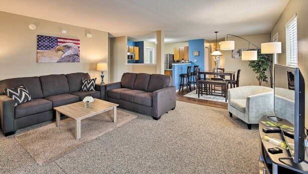 A living room with a dark brown sofa, a wooden coffee table, and a TV stand with a flat-screen TV. There is a dining area with a table and chairs in the background. - Patio Dining, 7 Mi to Purdue: Family Escape! (Lafayette)