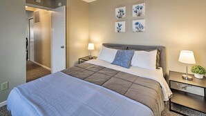 A hotel room with a large bed, two bedside tables, a wall-mounted lamp, and a door leading to a hallway. - Patio Dining, 7 Mi to Purdue: Family Escape! (Lafayette)