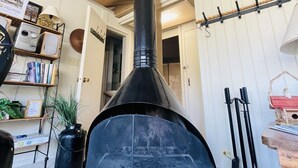 Una habitación con chimenea negra, vigas de madera, una estantería y un perchero.