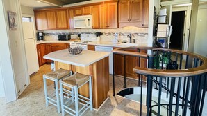 Una cocina con armarios de madera, una isla central, taburetes de bar y una escalera que sube a otro nivel.