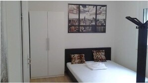 Ett sovrum med en säng, två kuddar, ett konstverk med en stadsbild på väggen och en garderob.