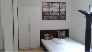 Een slaapkamer met een bed, twee kussens, een stadsgezicht aan de muur en een kledingkast.