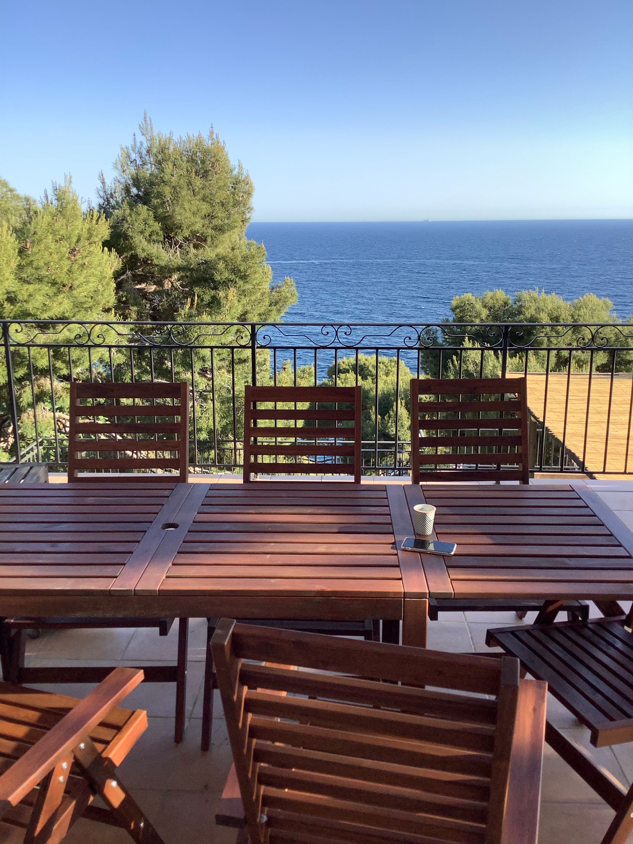 A wooden table and chairs on a balcony with a view of the sea.