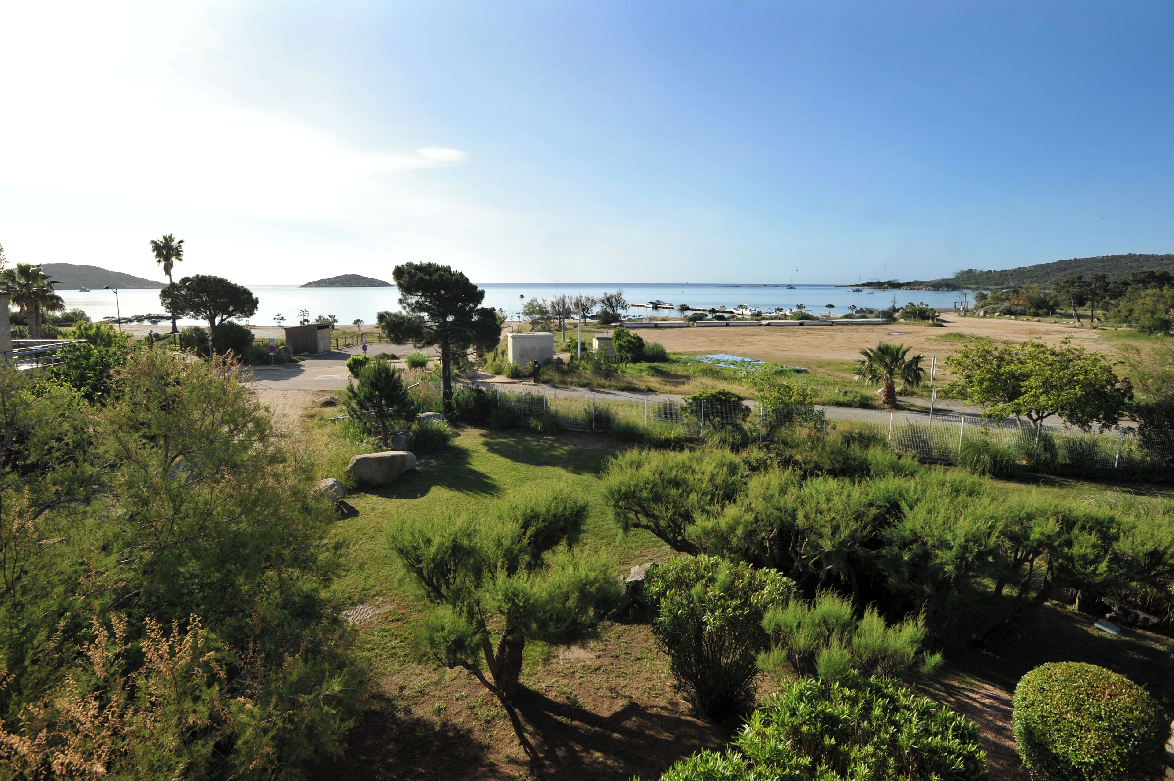 A coastal area with a parking lot, greenery, and a view of the sea.