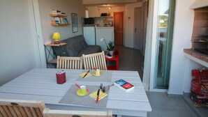 A dining area with a table set for two, a small kitchen in the background, and a sliding glass door leading to an outdoor area.