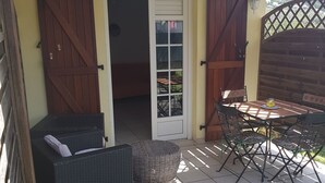 Eine überdachte Terrasse mit Tisch und Stühlen, einem Korbsessel und einem Holzboden.