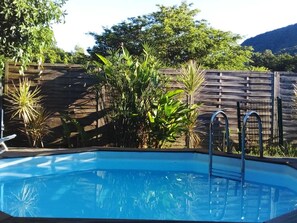Une piscine rectangulaire avec des échelles en métal, entourée d’une clôture en bois et agrémentée de diverses plantes.