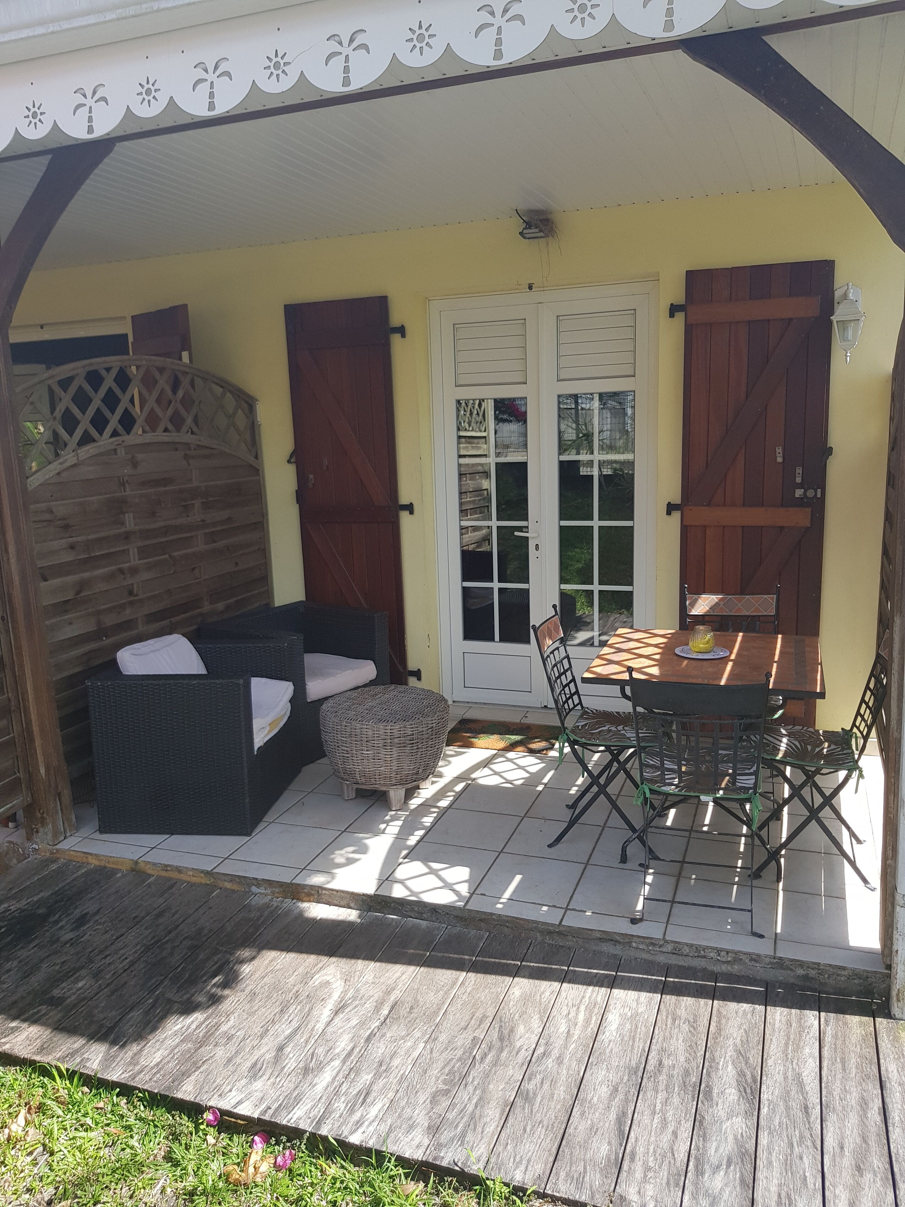 A covered patio with a dining table and chairs, a wicker sofa, and a wooden fence.