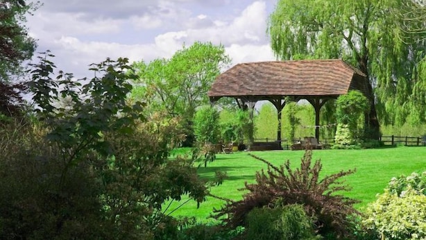 A pavilion with a tiled roof, surrounded by lush greenery and a small pond.
