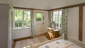 A bedroom with a bed, dresser, mirror, and large windows with curtains.