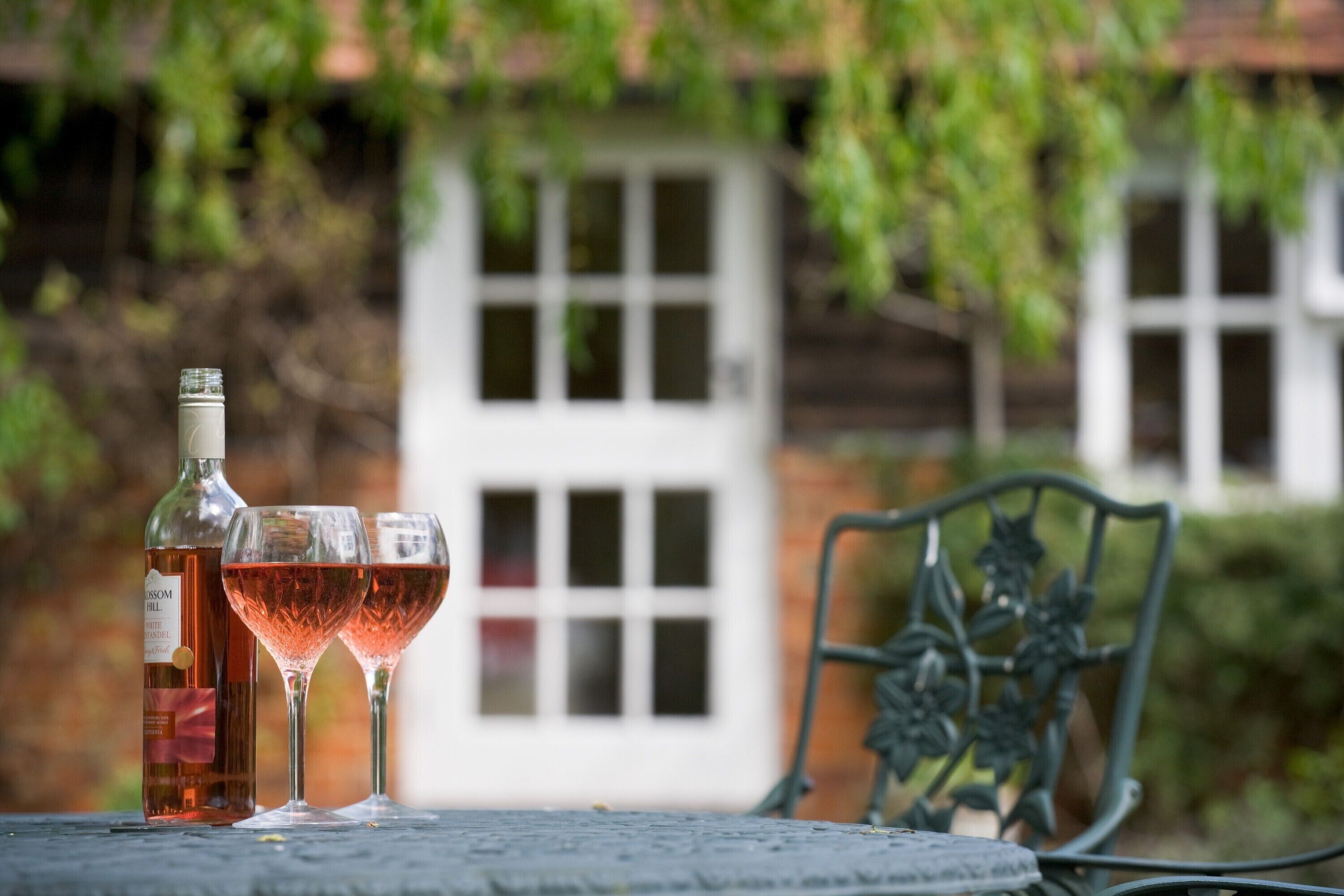 Eine Flasche Roséwein und zwei Gläser auf einem Tisch mit einem Metallstuhl in einem Garten.