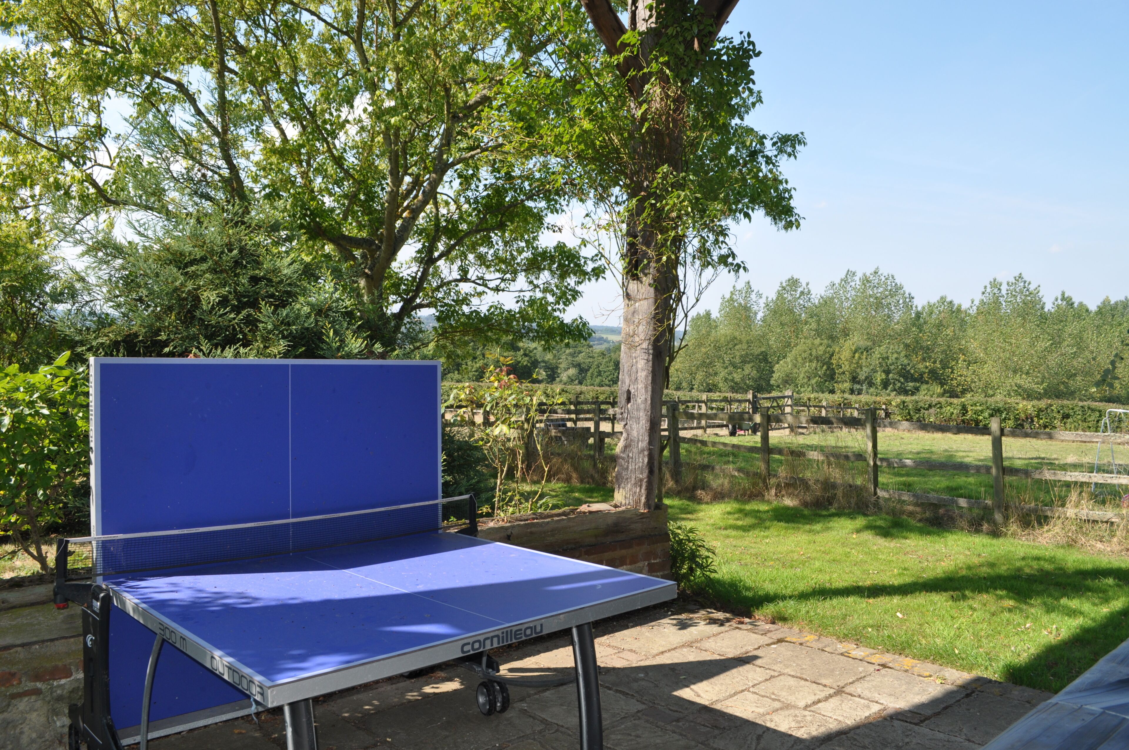 Een blauwe tafeltennistafel buiten, met een helder uitzicht op een landelijk landschap op de achtergrond.