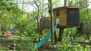 A treehouse with a slide, surrounded by dense greenery.