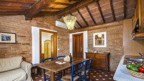 A cozy dining area with a wooden table and blue chairs, a beige sofa, and a kitchen area with a marble countertop. - Two-room apartment in residence with swimming pool and restaurant (Grosseto)