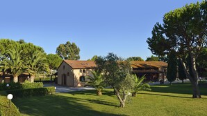 A building with a tiled roof, surrounded by well-maintained grass and trees. - Two-room apartment in residence with swimming pool and restaurant (Grosseto)