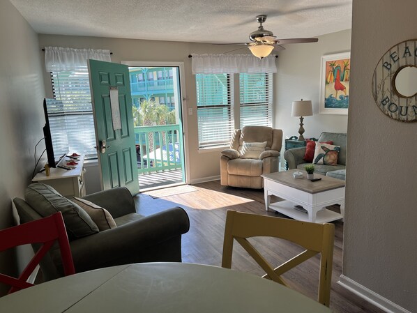 A cozy living room with a teal door, a beige armchair, a white coffee table, and a painting on the wall.