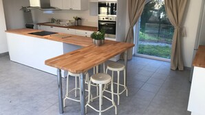 Une cuisine moderne avec un îlot central en bois, des armoires blanches, des appareils électroménagers en acier inoxydable et une vue sur un jardin grâce à une grande fenêtre.