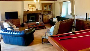 Un salon chaleureux avec une table de billard, une cheminée, un téléviseur et des fauteuils confortables.
