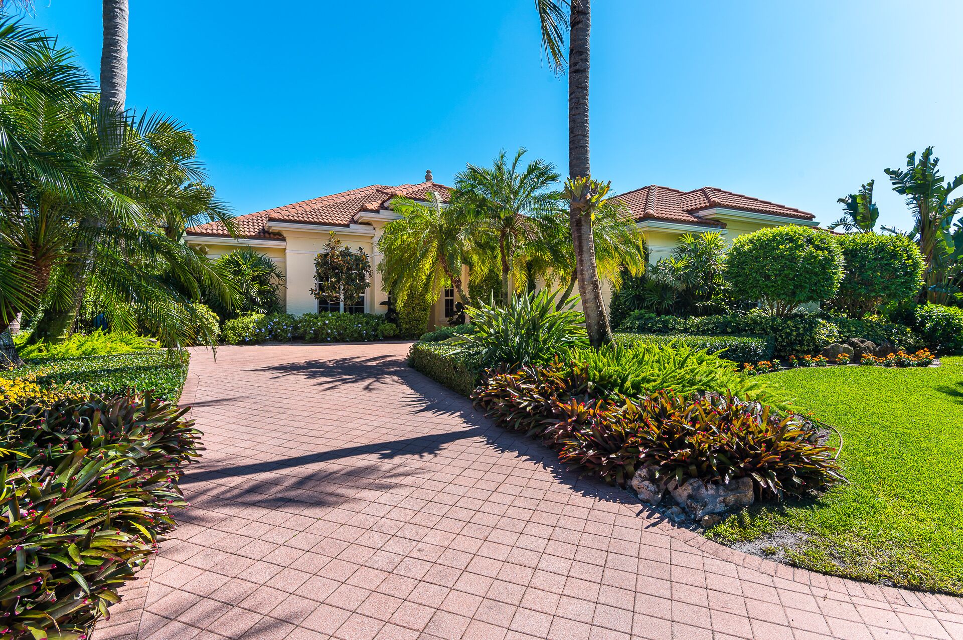 A pathway leading to a building with a tiled roof, surrounded by lush greenery and palm trees.