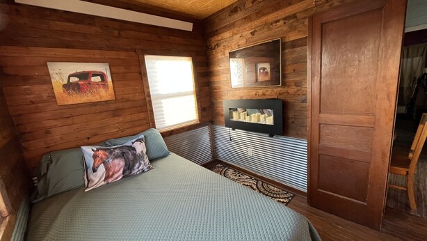 Une chambre aménagée dans une cabane en bois, avec un lit, une fenêtre, un miroir et des étagères fixées au mur.