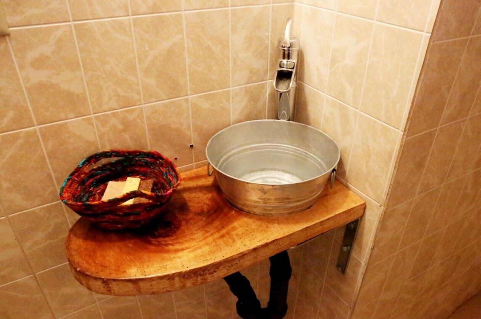 Un baño con un estante de madera que sostiene un lavabo metálico y una cesta de colores.