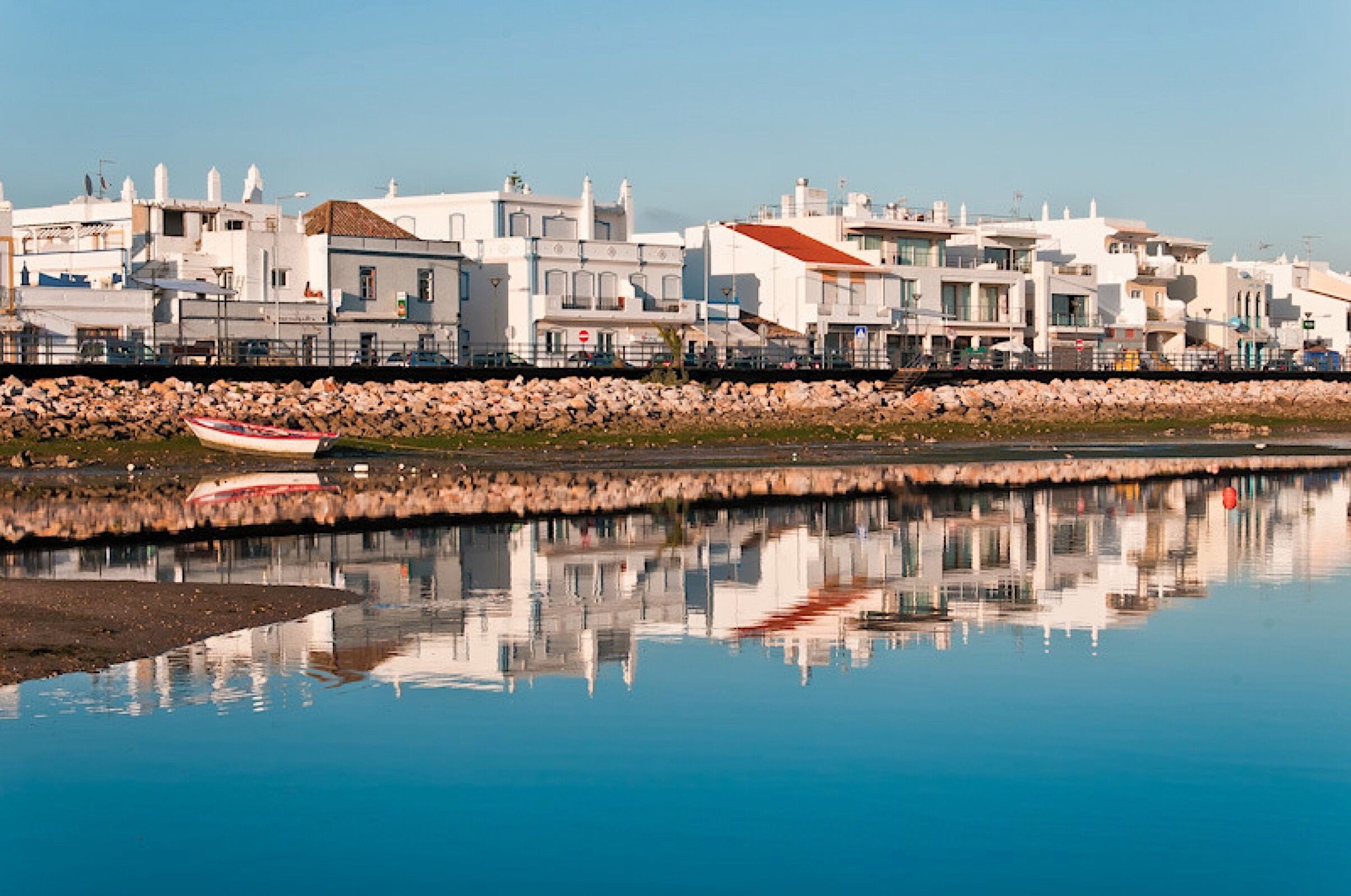 A coastal town with modern buildings, a calm waterfront, and a small boat docked near the shore.