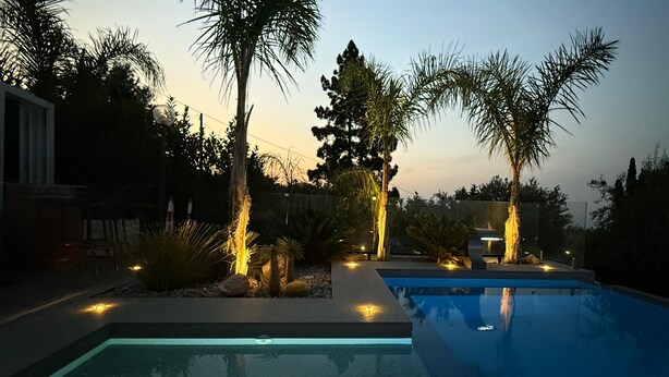 Una piscina con palmeras y una puesta de sol al fondo.