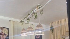 Comedor con mesa blanca, sillas negras, individuales tejidas, lámparas colgantes y una planta en maceta.