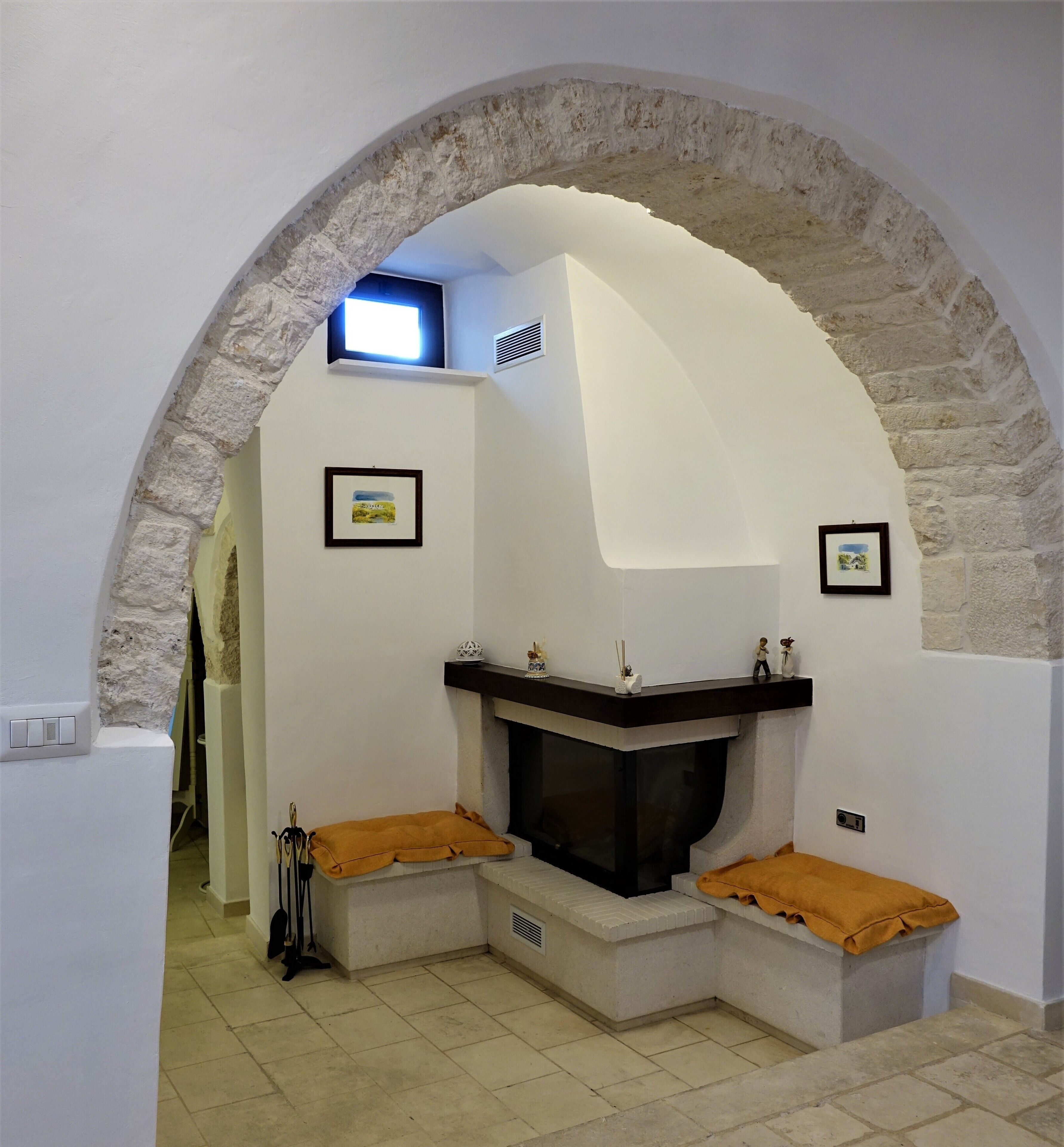 Una habitación con chimenea, arco de piedra y dos cuadros en la pared.