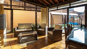 A covered patio area with wicker furniture, a glass table, and a television on a stand.