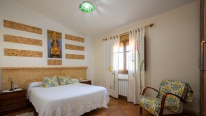 A bedroom with a bed, a chair, a nightstand, and a wall with artwork.