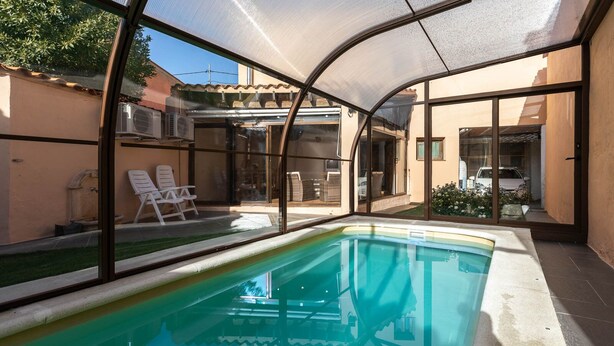 A swimming pool with a glass enclosure, surrounded by lounge chairs and a view of a residential area.