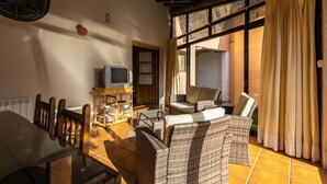 A cozy living room with wicker furniture, a television on a wooden stand, and a large window with curtains.