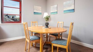 Uma sala de jantar com uma mesa redonda de madeira, quatro cadeiras, um vaso com flores e três quadros na parede.