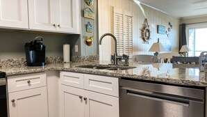 A modern kitchen with white cabinetry, granite countertops, stainless steel appliances, and decorative wall art. - Sea Oaks Oceanfront 2-Bed / 2-Bath (Garden City)